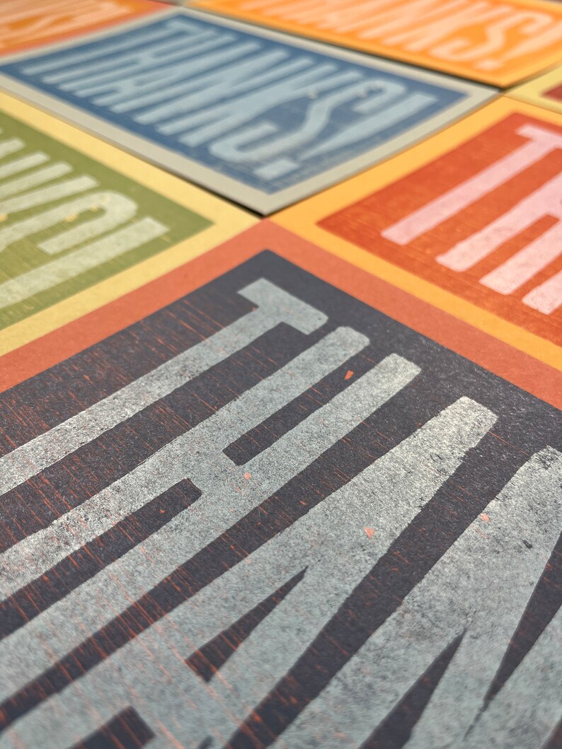 Puede incluir: Primer plano de un conjunto de tarjetas con diferentes colores y texturas. Cada tarjeta presenta una palabra en negrita, en blanco. Las palabras son "THANKS", "YOU'RE", "AMAZING", "I LOVE" y "THAT".