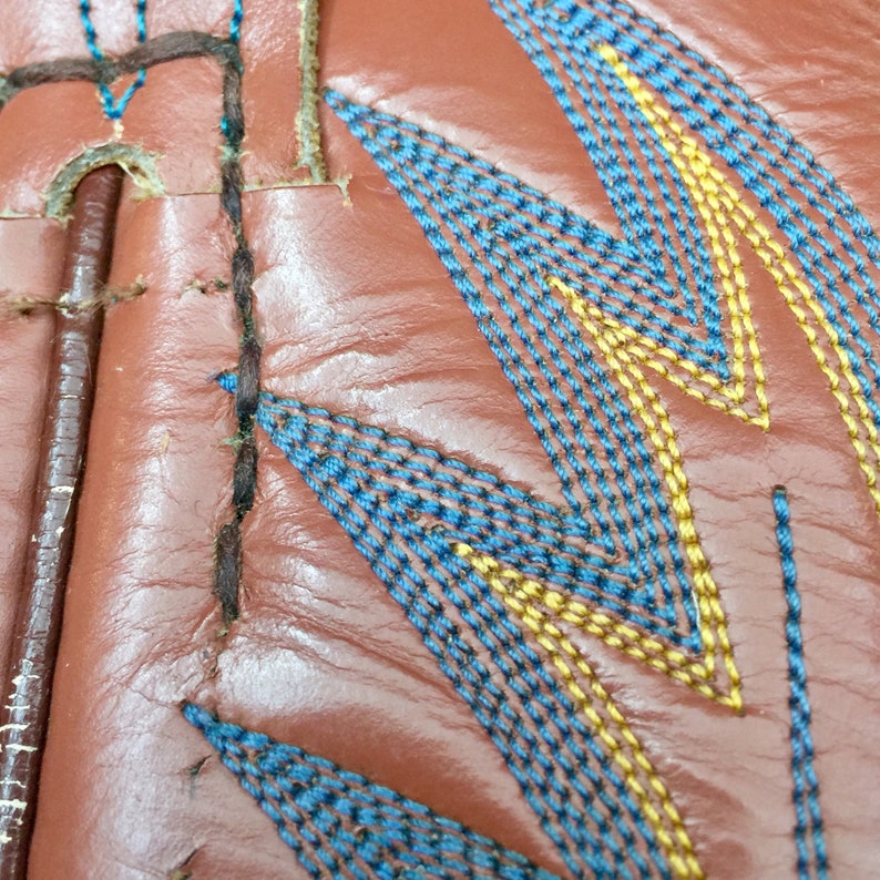May include: Close-up of brown leather with blue and yellow stitching in a zig-zag pattern.