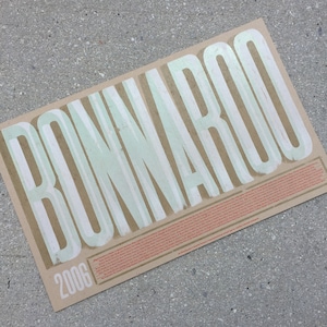 May include: A vintage-style poster for the 2006 Bonnaroo Music & Arts Festival. The poster features the festival name in large, white, stylized lettering on a brown background.