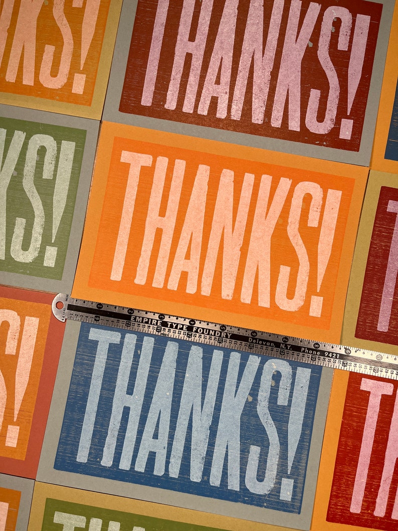 Puede incluir: Primer plano de un conjunto de tarjetas con la palabra "THANKS!" impresa en varios colores y estilos. Las tarjetas est&aacute;n dispuestas en una cuadr&iacute;cula y todas son del mismo tama&ntilde;o. Una regla se coloca encima de las tarjetas.