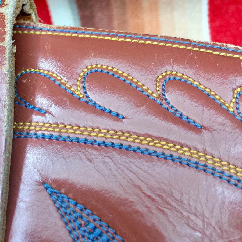 May include: Close-up of brown leather with blue and yellow stitching in a wavy pattern.