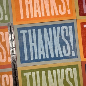 Puede incluir: Tres tarjetas con la palabra "THANKS!" impresa en blanco sobre fondos de colores diferentes. Las tarjetas son naranja, azul y verde.