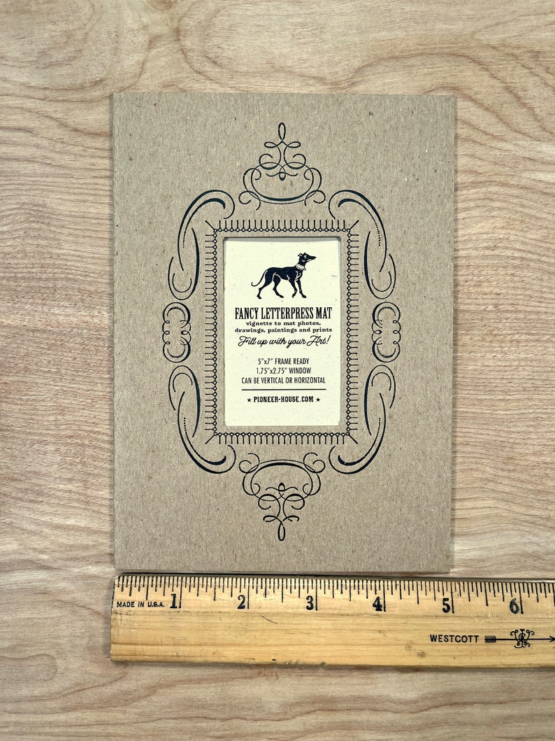 Peut inclure: Un tapis en carton brun avec un cadre orn&eacute; noir et une silhouette noire de chien &agrave; l'int&eacute;rieur. Le texte indique "Fancy Letterpress Mat" et "Fill up with your Art!" Le tapis mesure 5 pouces par 7 pouces et a une fen&ecirc;tre de 1,75 pouce par 2,75 pouce. Le tapis peut &ecirc;tre utilis&eacute; verticalement ou horizontalement. L'adresse du site Web est "pioneer-house.com".