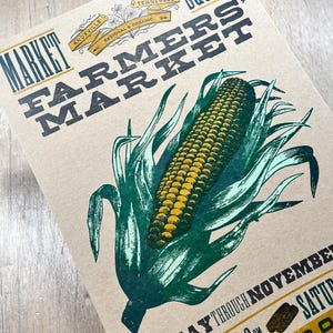 May include: A tan poster for the Knoxville Square Farmers' Market. The poster features a detailed illustration of an ear of corn with green leaves. Text includes "Market Farmers' Market" and market hours.