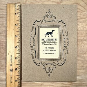 Peut inclure: Une carte marron avec un cadre orn&eacute; noir et une illustration noir et blanc d'un chien. Le texte indique "Fancy Letterpress Mat" et "Fill up with your Art!"  5"x7" Frame Ready, 1.75"x2.75" Window, Can be Vertical or Horizontal, Pioneer-House.com.