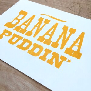 May include: A white card with the text "BANANA PUDDIN*" printed in yellow.