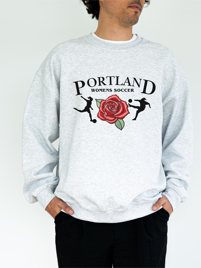May include: A grey sweatshirt with a graphic print of a rose and two football players. The text "PORTLAND WOMENS SOCCER" is printed above the graphic.