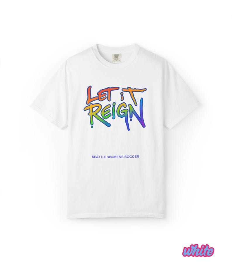 May include: White t-shirt with the text "LET IT REIGN" in rainbow colors. Below the text is "SEATTLE WOMENS SOCCER". The shirt has short sleeves and a crew neck.