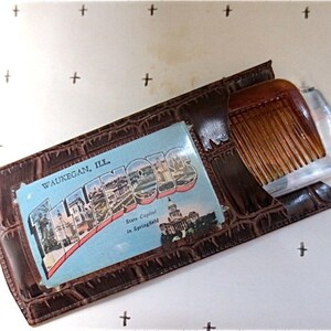 May include: A brown leather case with a postcard inside. The postcard shows a cityscape with the text "WAUKEGAN, ILL. State Capital in Springfield". The case also has a brown comb inside.