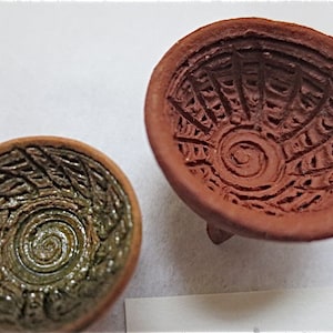 May include: Two small, round, terracotta bowls with decorative patterns. One bowl is brown with a spiral design, the other is green with a spiral design.