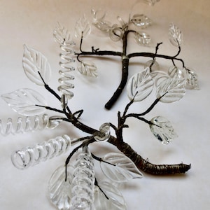 May include: Two decorative glass tree branches with clear glass leaves and coiled accents. The branches are brown and the leaves are clear, creating a delicate and artistic design. The leaves are approximately 3 inches long.