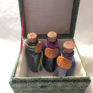May include: Three small glass bottles with cork stoppers and colorful wax seals inside a green fabric-covered box with a hinged lid.