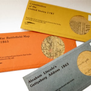 May include: Three envelopes with a circular window revealing a vintage document. The envelopes are yellow, orange, and gray. The text on the envelopes reads "Constitution of the United States 1787", "Civil War Battlefield Map 1861-1865", and "Abraham Lincoln's Gettysburg Address 1863".