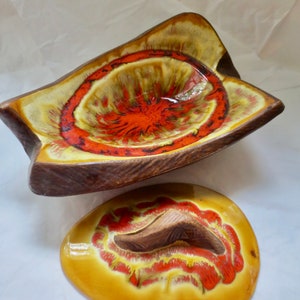 May include: A two-piece ceramic bowl set with a unique design. The bowl is a star-like shape with a brown rim and a yellow, orange, and red interior. The lid is oval-shaped, mirroring the bowl's color scheme. The set has a mid-century modern aesthetic.