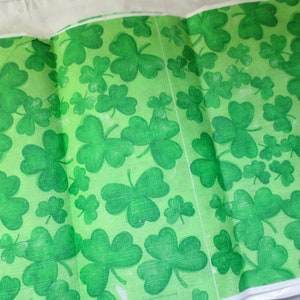 May include: Green fabric with a repeating pattern of shamrocks. The fabric is folded in half.