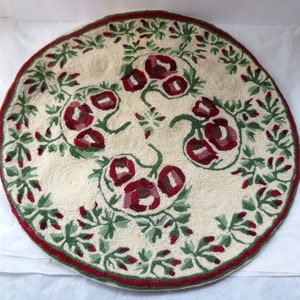 K&ouml;nnte beinhalten: Ein runder, cremefarbener Teppich mit einem roten und gr&uuml;nen Blumendesign. Der Teppich ist aus gewebtem Stoff und hat einen Fransenrand.