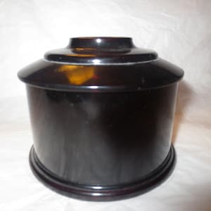 May include: A black, round, ceramic jar with a lid. The jar has a smooth, glossy finish.