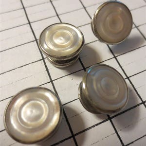 May include: Four silver and mother-of-pearl cufflinks. Each cufflink has a round, white mother-of-pearl center with concentric circles.