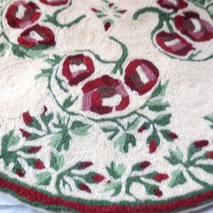 K&ouml;nnte beinhalten: Ein runder, cremefarbener Teppich mit einem roten und gr&uuml;nen Blumenmuster. Der Teppich hat einen roten Rand.