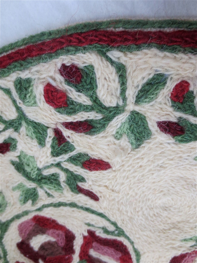 K&ouml;nnte beinhalten: Nahaufnahme eines cremefarbenen Teppichs mit rotem und gr&uuml;nem Blumendesign. Der Teppich hat einen roten Rand und ist aus weichem, flauschigem Material.
