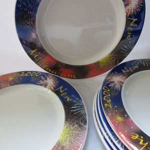 May include: A set of white ceramic plates with a blue, red, and yellow firework design around the rim. The plates have the text "New 2000 Millennium" in gold lettering.