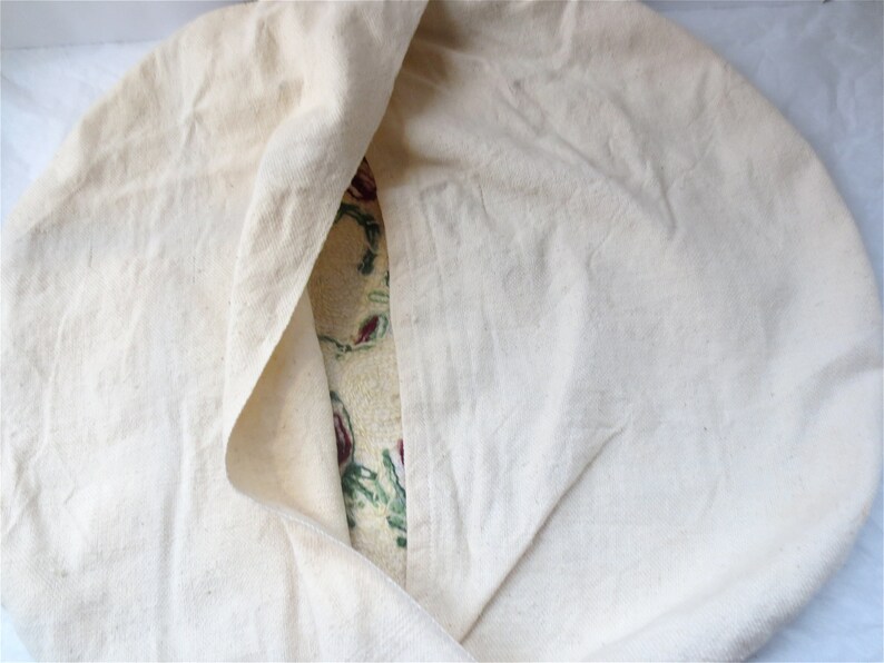 K&ouml;nnte beinhalten: Ein wei&szlig;er Baumwollstoff ist &uuml;ber einen Stoff mit floralem Muster gefaltet. Das Blumenmuster ist in den Farben Rot, Gr&uuml;n und Gelb gehalten.