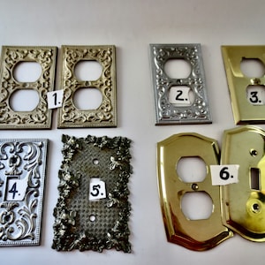 May include: Six decorative outlet and light switch covers in various styles and finishes. The covers are made of metal and have ornate designs. The covers are numbered 1 through 6.