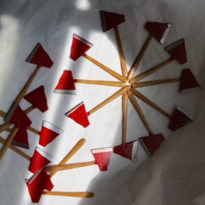 May include: A collection of small toy axes arranged in a circular pattern and scattered nearby. Each axe features a bright red head with a silver-colored blade edge and a light brown wooden handle. The items are displayed on a plain white surface.