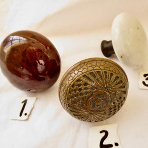 May include: Three vintage door knobs, one is brown, one is white, and one is brass with a decorative design. The knobs are numbered 1, 2, and 3.