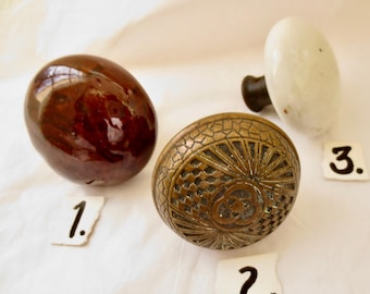 Pode incluir: Três maçanetas de porta vintage, uma é marrom, outra é branca e outra é de latão com um design decorativo. As maçanetas são numeradas de 1 a 3.