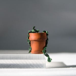 Miniature potted ivy plant monitor topper made out of polymer clay. The plant is dark green with some lighter green leaves. The pot is terra cotta.