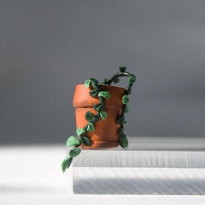 Miniature potted ivy plant monitor topper made out of polymer clay. The plant is dark green with some lighter green leaves. The pot is terra cotta.