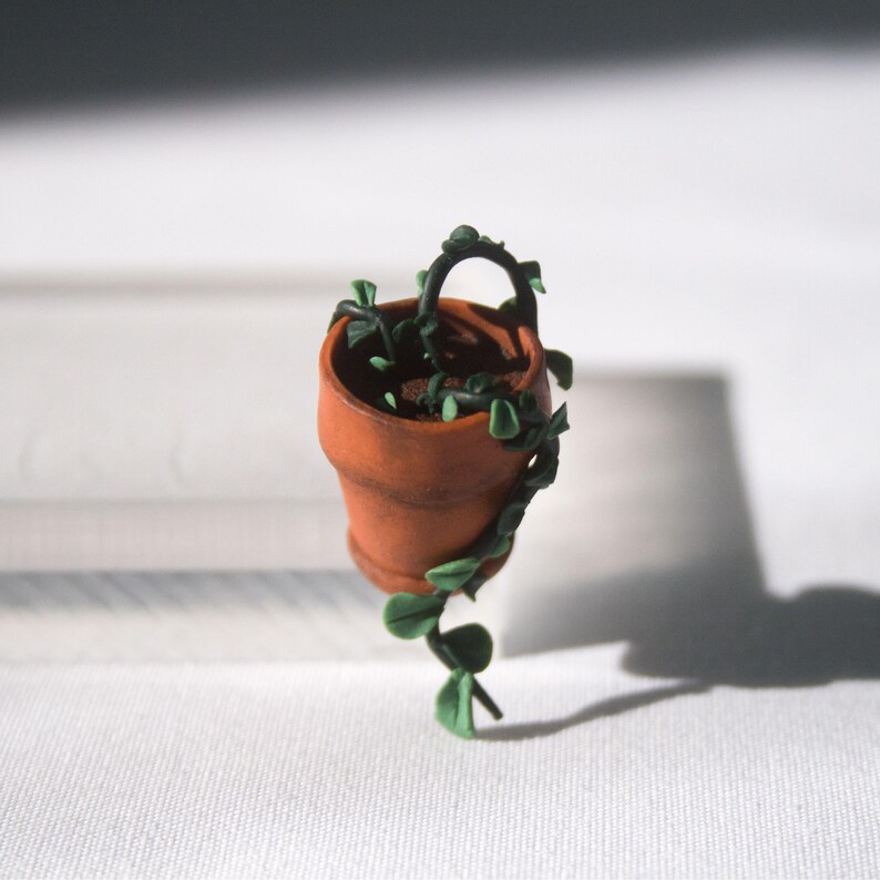 Miniature potted ivy plant monitor topper made out of polymer clay. The plant is dark green with some lighter green leaves. The pot is terra cotta.