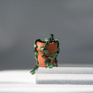 Miniature potted ivy plant monitor topper made out of polymer clay. The plant is dark green with some lighter green leaves. The pot is terra cotta.