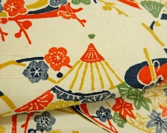 May include: Close-up of a cream-colored fabric with a repeating Japanese-inspired pattern. The design features red, yellow, blue, and green floral and geometric elements. The fabric has a textured appearance.