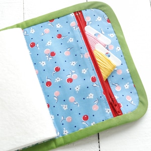May include: A green fabric zippered pouch with a blue and white cherry print lining. The pouch is open and has three spools of embroidery floss inside.