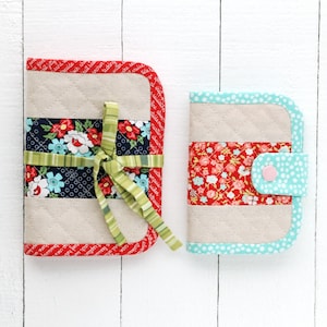 May include: Two quilted fabric zippered pouches with a floral print and a light blue trim. The larger pouch has a green ribbon tied around it. The smaller pouch has a pink button.