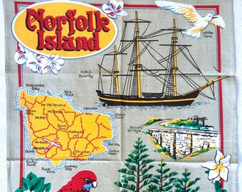 Puede incluir: Un paño de cocina vintage con un mapa de la isla Norfolk, Australia. El mapa muestra varios puntos de referencia, incluyendo el monte Pitt, la bahía Cascade y el puente Bloody. El paño de cocina también presenta un barco, un pájaro y un árbol.