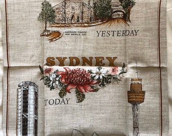 Puede incluir: Un paño de cocina de lino vintage con un diseño que presenta monumentos emblemáticos de Sídney, Australia. La mitad superior del paño muestra edificios históricos con el texto "Yesterday" y la mitad inferior muestra edificios modernos con el texto "Today". El texto "Sydney" está impreso en letras grandes en el centro del paño.