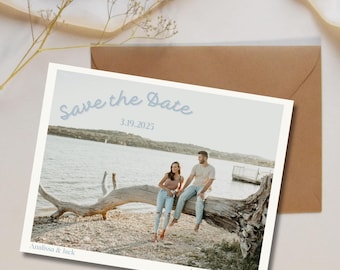Puede incluir: Tarjeta "Save the Date" con una foto de una pareja sentada en un tronco junto a un lago. El texto de la tarjeta dice "Save the Date" en letra cursiva azul, "3.19.2025", "Analissa & Rick" y "Lake Tahoe, California".