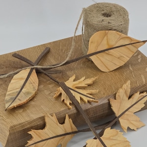 May include: A wooden box with several wooden leaf decorations and a spool of twine. The leaves are light brown with dark brown veins and stems. The box is made of light brown wood.