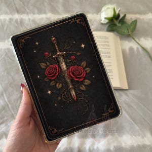 May include: A rectangular tablet case featuring a black background with a central illustration of a silver sword entwined with thorny vines and two large red roses. The design includes small gold stars and decorative corner flourishes.