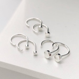 May include: A set of three silver hoop earrings with a small round disc at the end of each hoop.