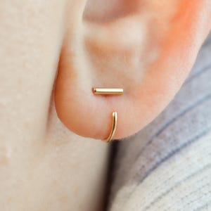 May include: A pair of gold earrings, one is a small hoop and the other is a straight bar.