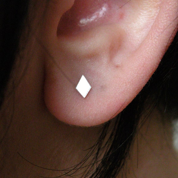May include: A close-up of a person's ear with a small, diamond-shaped earring. The earring is made of silver and is a simple, minimalist design.