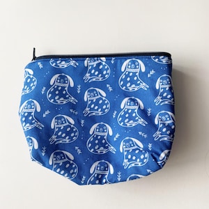 Könnte beinhalten: Eine blaue Reißverschlusstasche mit einem weißen Muster aus stilisierten Hunden. Die Hunde sind alle nach vorne gerichtet und haben ein gepunktetes Muster.