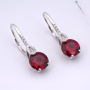 May include: A pair of silver dangle earrings with a red gemstone and a small diamond accent.