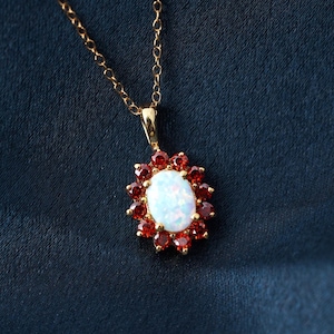 Puede incluir: Un collar de cadena de oro con un colgante que presenta una opala blanca rodeada de piedras preciosas rojas.