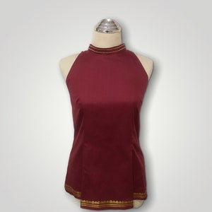 May include: A maroon sleeveless top with a high neckline and gold trim around the neck and hem.