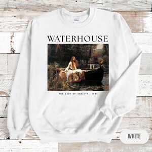 May include: White sweatshirt with a print of a painting by John William Waterhouse titled "The Lady of Shalott, 1888". The painting depicts a woman in a boat on a river.
